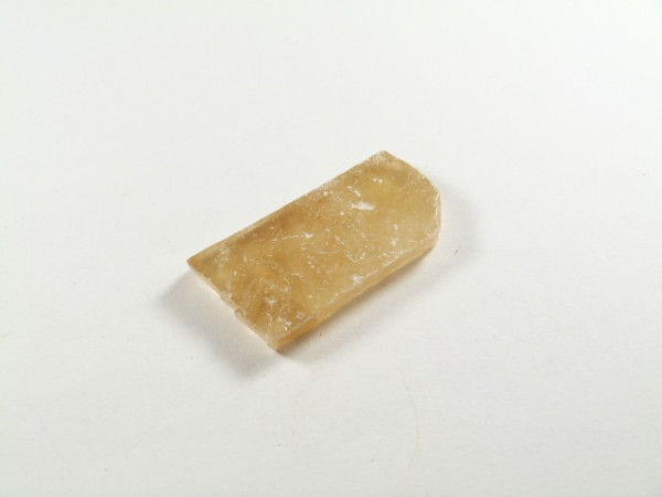 Kalcyt złoty/ kalcyt złocisty - kamień naturalny, surowy, nieszlifowany. Prostokątny kawałek jasnobrązowego kamienia leży na białym tle.