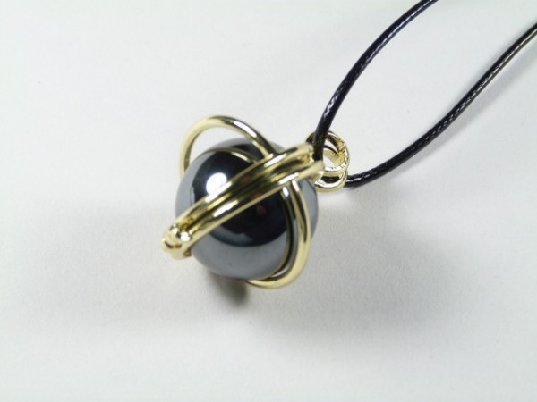 Wisiorek z czarną kulą otoczoną złotymi obręczami na czarnym sznurku.