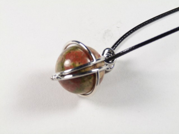 Wisiorek z kamieniem w kształcie kuli, opleciony metalowym drutem, na czarnym sznurku.