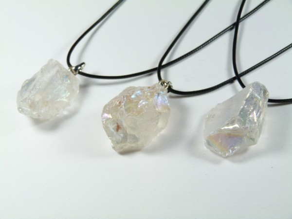 Trzy naszyjniki z surowymi, przezroczystymi kryształami na czarnych sznurkach.