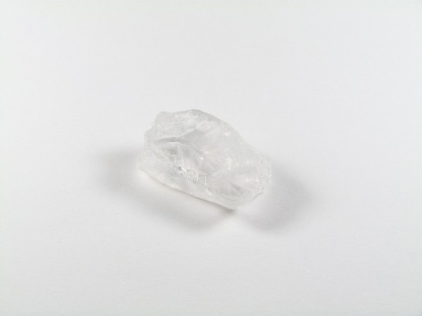 Przezroczysty kryształ kwarcu leży na białym tle.