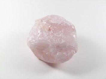Różowy, surowy kryształ kwarcu na białym tle.