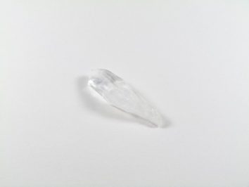 Przezroczysty kryształ kwarcu leży na białym tle.