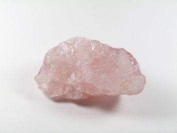 Różowy, surowy kryształ kwarcu leży na białym tle.