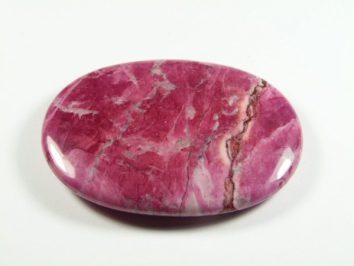 Howlit różowy - kamień gładzony, polerowany, szlifowany. Różowy, wypolerowany kamień o owalnym kształcie na białym tle.