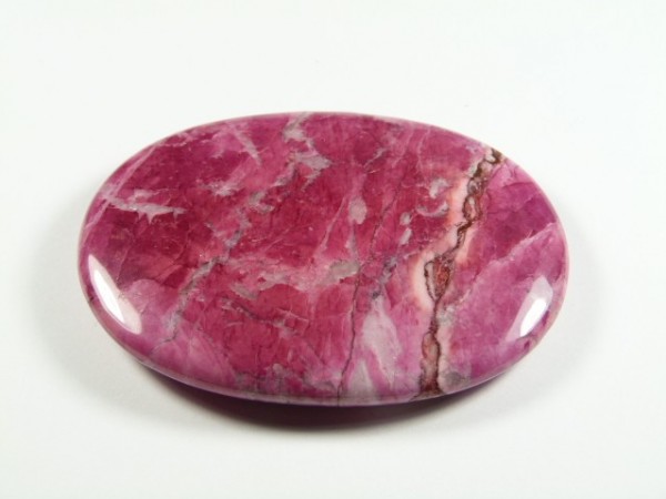 Howlit różowy - kamień gładzony, polerowany, szlifowany. Różowy, wypolerowany kamień o owalnym kształcie na białym tle.