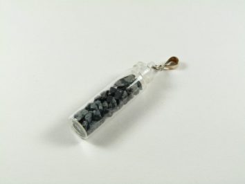 Mała fiolka z czarnymi kamieniami, zamknięta i zawieszona na metalowym uchwycie.