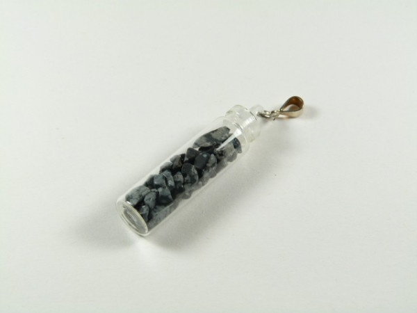 Mała fiolka z czarnymi kamieniami, zamknięta i zawieszona na metalowym uchwycie.