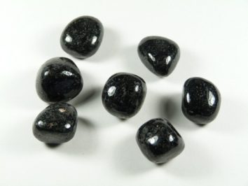 Siedem czarnych, polerowanych kamieni leży na białym tle.
