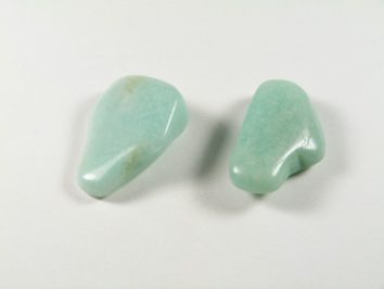 Dwa gładkie, jasnoniebieskie kamienie amazonitu leżące na białym tle.