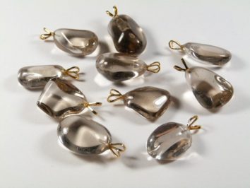 Dziesięć przezroczystych wisiorków z kamieni z metalowymi zawieszkami leży na białym tle.
