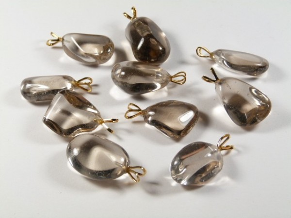 Dziesięć przezroczystych wisiorków z kamieni z metalowymi zawieszkami leży na białym tle.