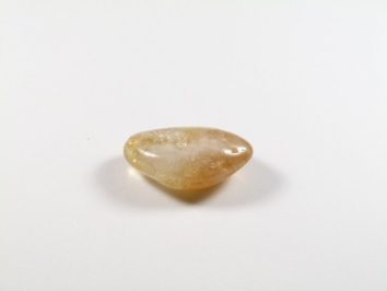 Polerowany kamień w kolorze jasnego żółtego leży na białym tle.