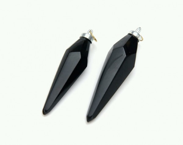 Dwa czarne, szpiczaste wisiorki z oczkami do zawieszenia, leżące na białym tle.