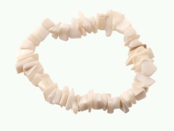 Bransoletka z białych, nieregularnych koralików ułożona w okrąg na jasnym tle.