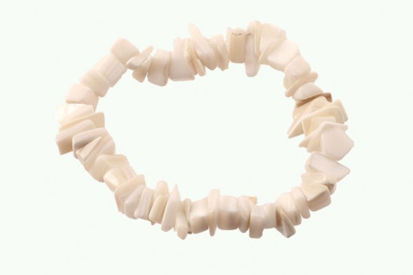 Bransoletka z białych, nieregularnych koralików ułożona w okrąg na jasnym tle.