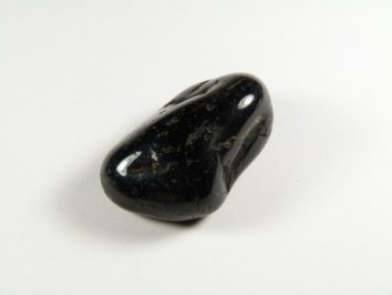 Czarny, wypolerowany kamień leży na białym tle.