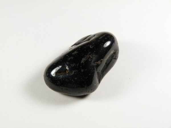 Czarny, wypolerowany kamień leży na białym tle.