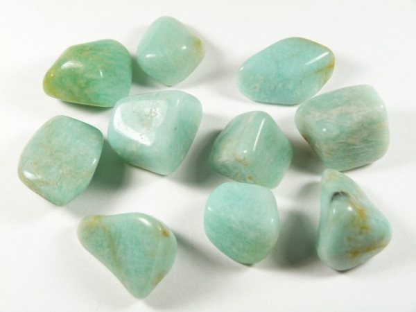 Dziesięć wypolerowanych, jasnozielonych kamieni amazonitu leży na białym tle.