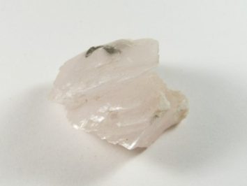 Kalcyt biały - kamień naturalny, surowy, nieszlifowany. Jasnoróżowy kryształ minerału leżący na białym tle.