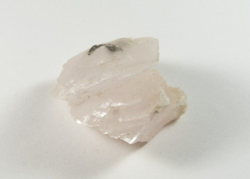 Kalcyt biały - kamień naturalny, surowy, nieszlifowany. Jasnoróżowy kryształ minerału leżący na białym tle.