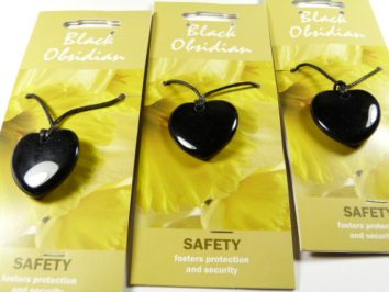 Trzy czarne wisiorki z obsydianu w kształcie serca na żółtych kartonikach z napisem „SAFETY”.