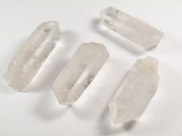 Cztery przezroczyste kryształy kwarcu leżące na białym tle.