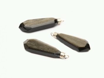 Trzy czarne, szlifowane zawieszki z kamienia na jasnym tle.