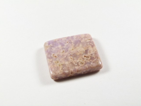 Polerowany, prostokątny kamień o jasnofioletowym zabarwieniu na białym tle.