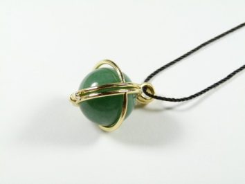 Wisiorek z zielonym kamieniem w złotej oprawie na czarnym sznurku, na białym tle.