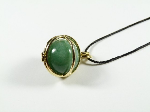 Wisiorek z zielonym kamieniem w złotej oprawie na czarnym sznurku, na białym tle.