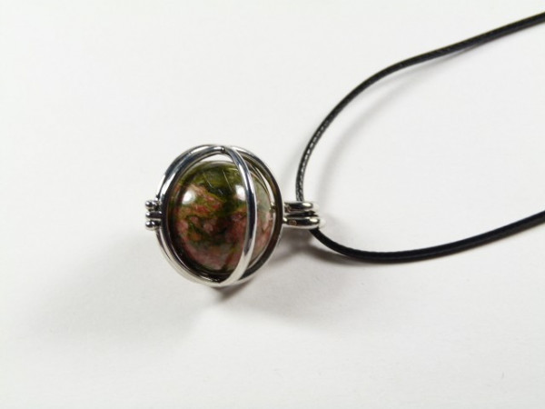 Wisiorek z kamieniem w metalowej oprawie na czarnym sznurku, na białym tle.