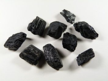 Osiem czarnych, błyszczących kamieni turmalinu leży na jasnym tle.