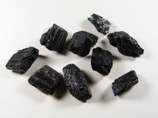 Osiem czarnych, błyszczących kamieni turmalinu leży na jasnym tle.