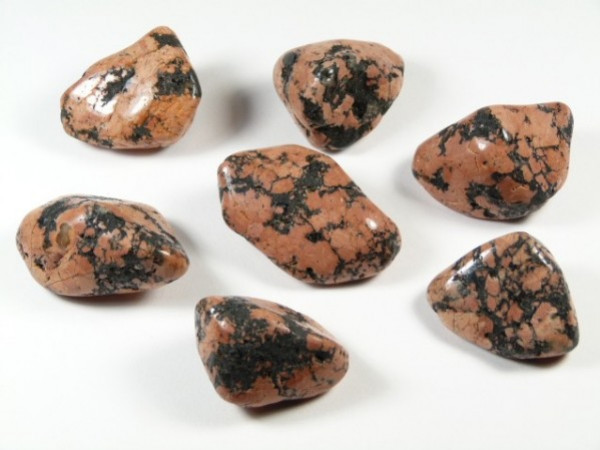 Siedem wygładzonych kamieni rodonitu z czarnymi żyłkami, leżących na białym tle.