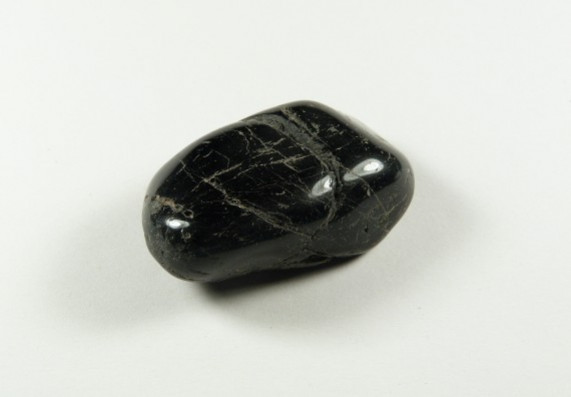 Czarny, wypolerowany kamień na białym tle, widoczny z góry.