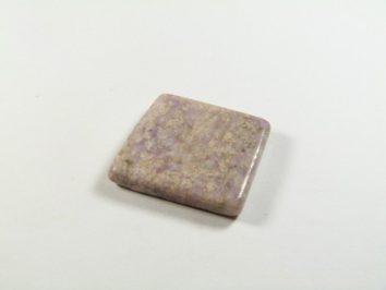 Kwadratowy, polerowany kamień o jasno fioletowym odcieniu leży na białym tle.