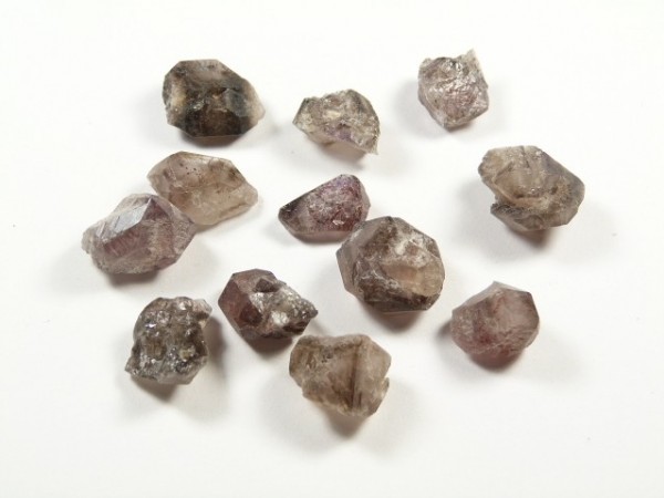 Lepidokrocyt - kamień naturalny, surowy, nieszlifowany. Dwanaście surowych kryształów leży na białym tle.