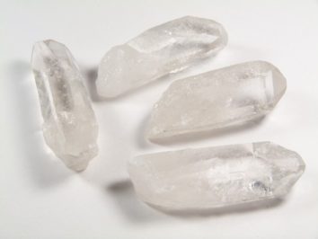 Cztery przezroczyste kryształy kwarcu leżące na białym tle.