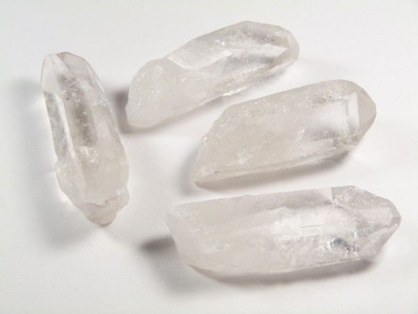 Cztery przezroczyste kryształy kwarcu leżące na białym tle.