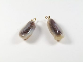 Dwa wisiorki z agatów w odcieniach brązu i bieli na białym tle.