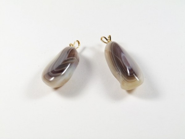 Dwa wisiorki z agatów w odcieniach brązu i bieli na białym tle.