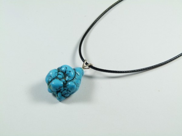 Naszyjnik z czarnym sznurkiem i niebieskim kamieniem o nieregularnym kształcie.
