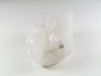 Biały, półprzezroczysty kamień kwarcu leży na jasnym tle.