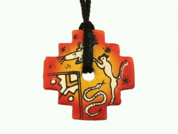 Wisiorek w kształcie krzyża z indiańskimi malunkami zwierząt na czerwonym i żółtym tle.