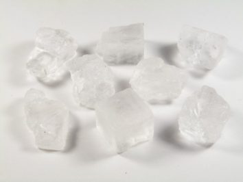 Kilka białych kryształków soli kamiennej leży na białym tle.