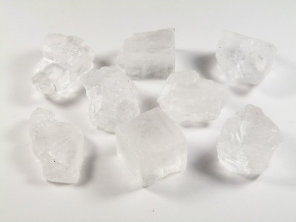 Kilka białych kryształków soli kamiennej leży na białym tle.