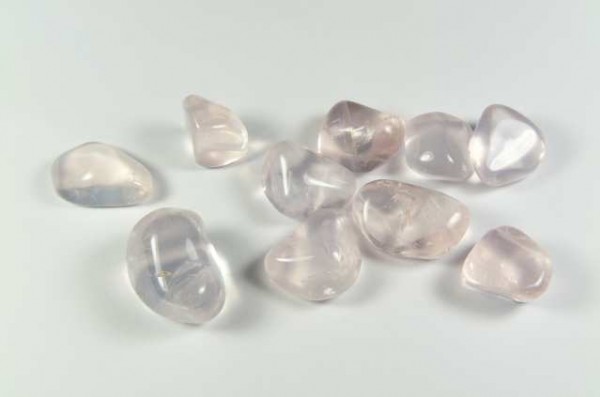 Dziesięć polerowanych kamieni różowego kwarcu leży na białym tle.