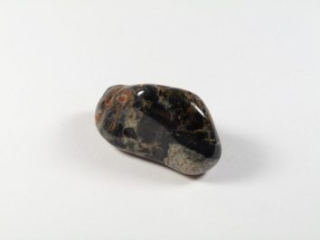 Wypolerowany, ciemny kamień z jasnymi i brązowymi żyłkami na białym tle.