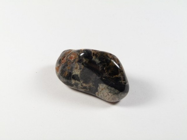 Wypolerowany, ciemny kamień z jasnymi i brązowymi żyłkami na białym tle.